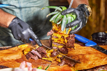Close-up of a chef slicing through grilled meat and pineapple using a sharp knife, showcasing culinary skill and precision.の写真素材