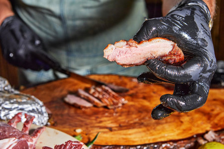 A gloved hand holds a freshly grilled meat slice, showing its tender and juicy texture on a wooden table.の写真素材