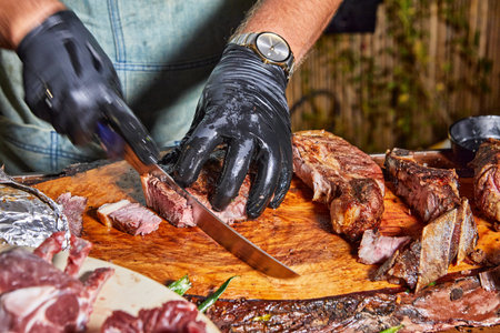 A chef uses a sharp knife to expertly cut through a thick piece of grilled beef on a wooden board, displaying precision.の写真素材