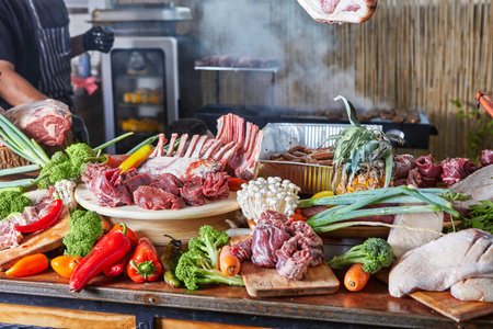 A vibrant display of raw meats, vegetables, and spices, ready for cooking and grilling, set on a rustic table.の写真素材