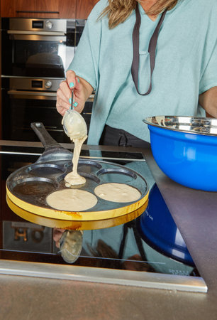 A person pours pancake batter into a round pancake mold on a stove, starting the cooking process for breakfast.の写真素材