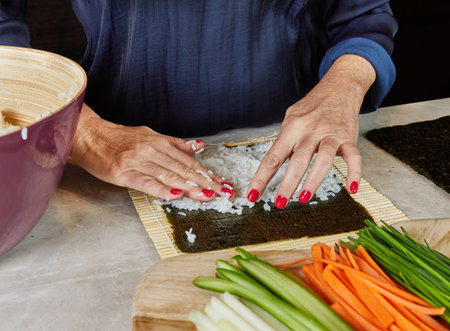 Hands carefully rolling sushi with a bamboo mat, combining fresh ingredients into a delicious Japanese delicacy.の写真素材