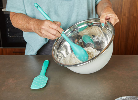 A person uses a spoon to mix flour and sugar in a bowl during the baking process, reflecting homemade preparation.の写真素材
