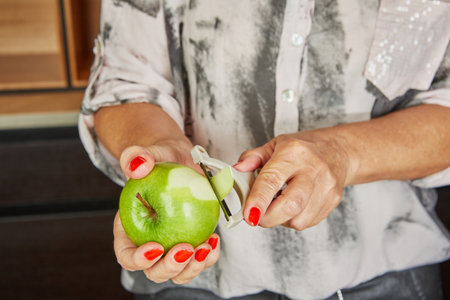 A person peels a green apple with a handheld peeler, preparing fruit for use in baking or cooking.の写真素材