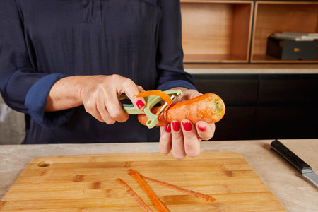Close-up of hands peeling a vibrant carrot on a wooden cutting board, highlighting precision and...
