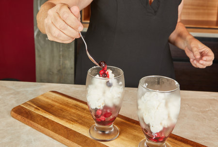A woman layering fresh berries over creamy dessert in glasses, crafting a delightful and colorful dessert presentation.の写真素材