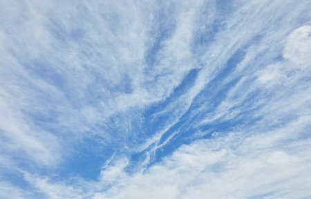A vibrant blue sky filled with delicate wispy white clouds, forming a dramatic natural pattern in...