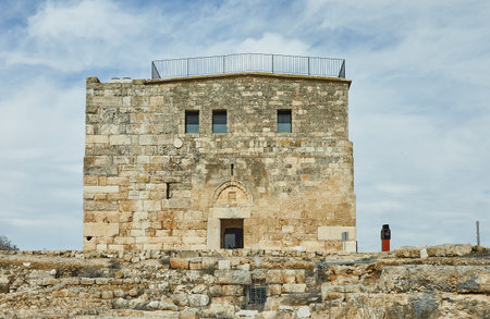An ancient stone fortress with partially ruined walls, standing under a bright blue sky, showing...