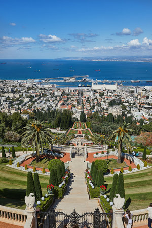 A grand stairway in Baha'i Gardens leads to the shrine, framed by vibrant flowers, trimmed bushes, and a panoramic port view.の写真素材