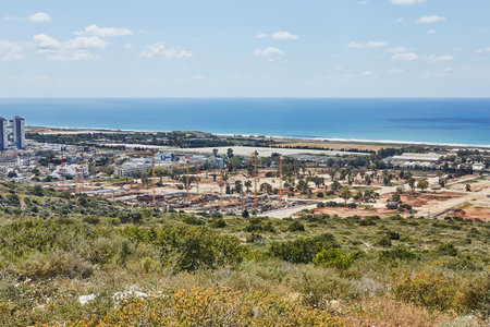 Seaside construction site with numerous cranes and buildings under development near the Mediterranean, surrounded by green natureの写真素材