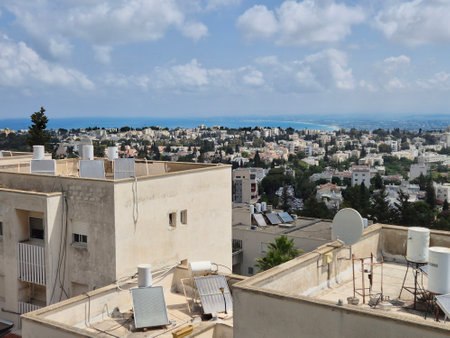 Scenic rooftop view of white buildings and residential blocks with a backdrop of sea and distant blue skyline under partly cloudy skiesの写真素材