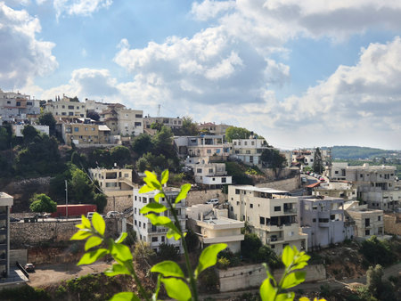Leafy foreground frames a hillside town of clustered white buildings rising above terraced slopes and winding roadsの写真素材