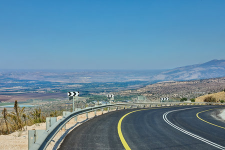 Curved mountain road with guardrails and directional signs, offering a panoramic view over the valley below.の写真素材