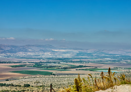 Farmland view with geometric crop fields, village buildings, and mountain backdrop under a blue skyの写真素材