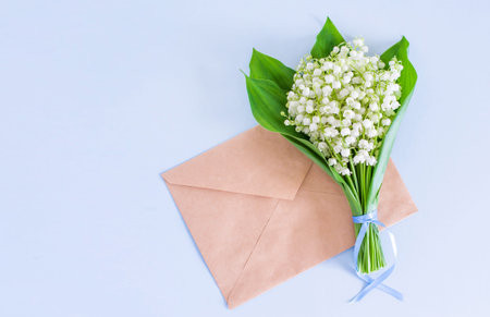 A bouquet of lilies of the valley on a blue background, tied with a ribbon and an envelope from...