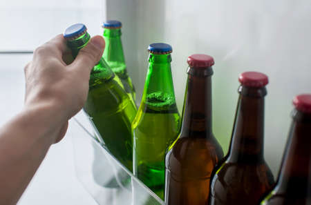 Male hand takes a bottle of beer from the refrigerator doorの写真素材