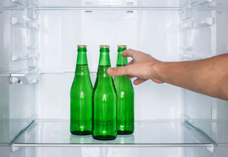 Man's hand reaches for a bottle of beer in the fridgeの写真素材