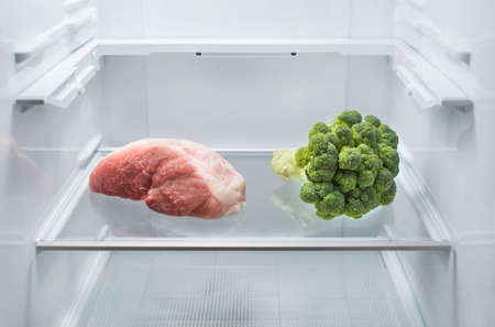 Fresh meat and broccoli opposite each other in an empty refrigerator. The choice between vegetarianism and meat-eatingの写真素材