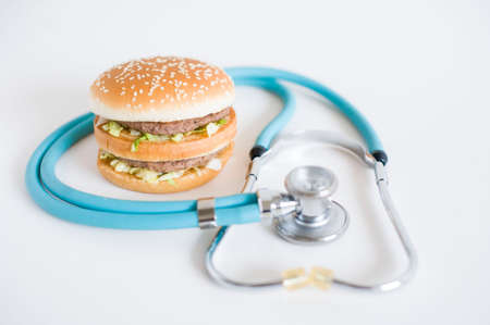 Hamburger and medical stethoscope on a white background. Health effects of junk foodの写真素材