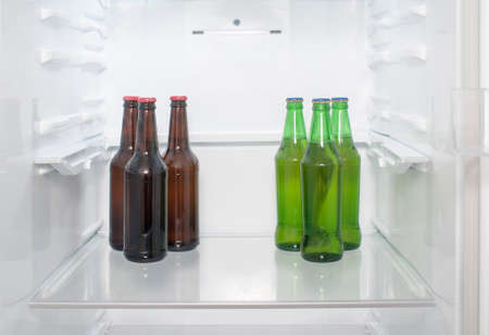 Green and brown glass beer bottles stand on a shelf in the refrigeratorの写真素材