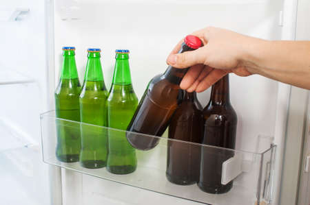 Male hand takes a bottle of beer from the refrigerator doorの写真素材