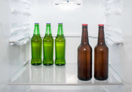 Green and brown glass beer bottles stand on a shelf in the refrigerator.の写真素材