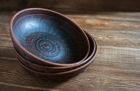 Handmade red clay clay plates lay on top of each other on a rough wooden tableの写真素材