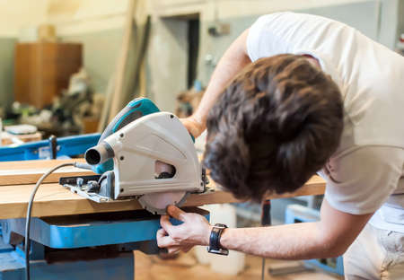 A man in a carpentry shop adjusts and checks a circular saw before workの写真素材