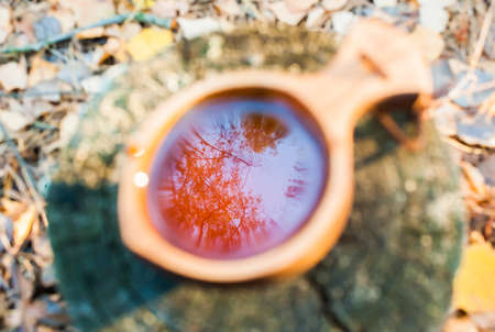 Tea in a wooden national mug "Kuksa" in the autumn forest. Reflection of the sky. Defocusの写真素材
