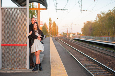 A young guy and a girl are standing and hugging on the railway platform. Evening, sunset