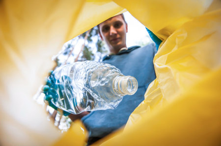 Garbage collection in nature. Young man puts plastic trash in a yellow bag, inside view