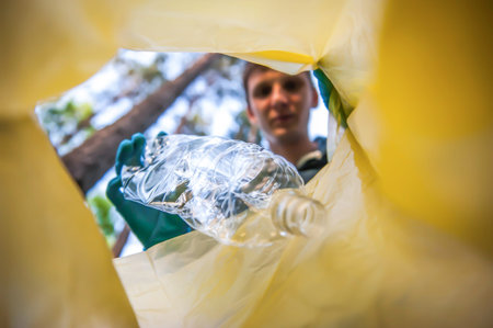 Garbage collection in nature. Young man puts plastic trash in a yellow bag, inside view