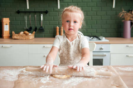 Happy mother and her little daughter knead dough together at home in the kitchen. Little girl helping mom to cook in the kitchenの写真素材