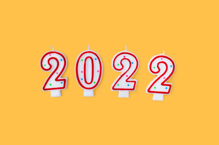 Red and white candle numbers 2022 and donut on red background. View from above. Christmas and New...
