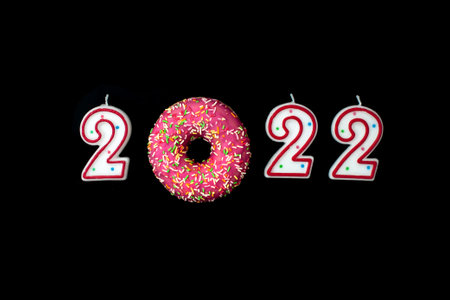 Red and white candle numbers 2022 and donut on red background. View from above. Christmas and New...
