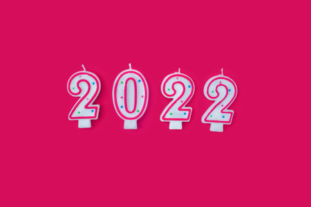 Red and white candle numbers 2022 and donut on red background. View from above. Christmas and New...