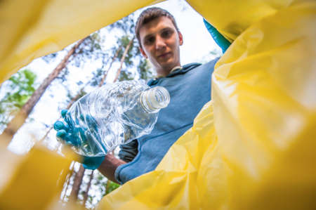 Garbage collection in nature. Young man puts plastic trash in a yellow bag, inside viewの写真素材