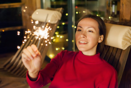 Young happy girl with sparkler in the evening on the terrace of the house. Holiday christmas and new year. defocusの写真素材