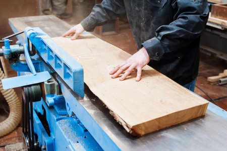 A male carpenter works in a carpentry workshop on a thickness gauge. planning wood