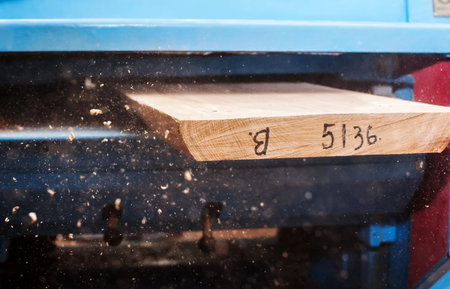 Male carpenter sawing a board with a circular saw in a carpentry workshop close-up