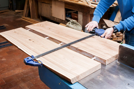Male carpenter sawing a board with a circular saw in a carpentry workshop close-up