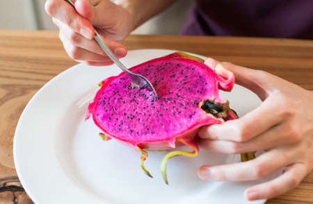 The girl holds in her hands a cut dragon fruit pitahaya at home in the kitchen close-up. soft focusの写真素材