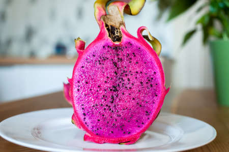The girl holds in her hands a cut dragon fruit pitahaya at home in the kitchen close-up. soft focusの写真素材