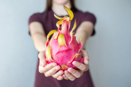 Girl with a spoon eats dragon fruit pitahaya at home in the kitchen close-upの写真素材