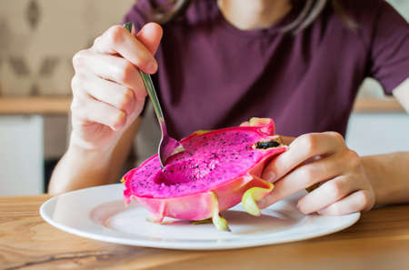 Girl with a spoon eats dragon fruit pitahaya at home in the kitchen close-upの写真素材
