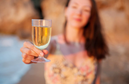 Girl holding a glass of white wine by the sea at sunsetの写真素材
