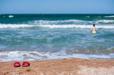 Sandals on a sandy beach against the backdrop of the sea, waves and a bathing woman. Defocusの写真素材