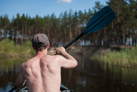 male tourist swims in a kayak in the summer along the river against the backdrop of a pine forest, rear viewの写真素材