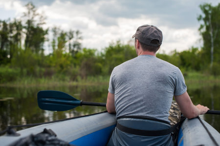 male tourist swims in a kayak in the summer along the river against the backdrop of a forest, rear...