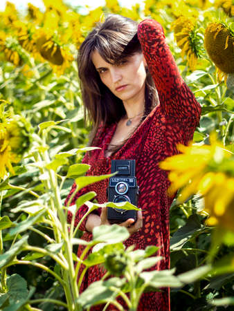A charming woman in a red dress takes a photo in a field with sunflowers.の写真素材